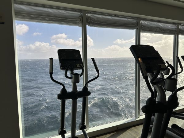 Crosstrainer vor der Fensterfront des Fitnessbereichs, dahinter aufgewühlte See.