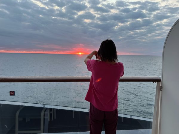 Kathi steht an der Reling und fotografiert den Sonnenaufgang über dem offenen Meer.